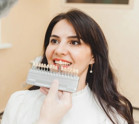 Dentist comparing tooth shade guide with patient for dental veneers treatment in Carthage