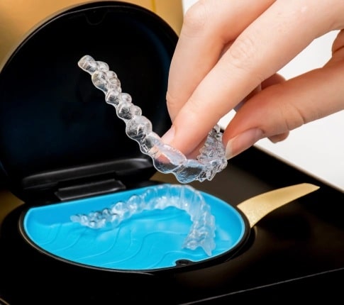 Hand holding clear Invisalign aligners above a dental case during teeth straightening treatment in Carthage