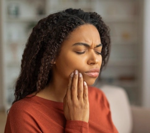 Woman holding jaw in pain from severe toothache needing emergency dental care in Carthage